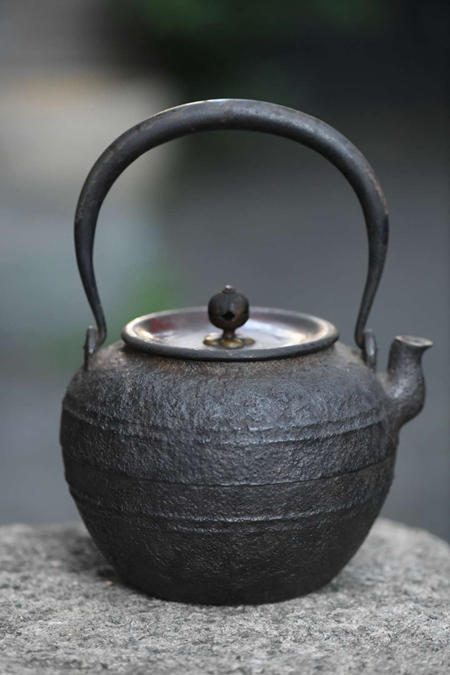 忠三郎 老铁壶
紫金堂名人忠三郎的作品极富巧趣，在百年后的今日仍吸引众多爱壶人士竞相收藏。 在众多铁壶作品中，紫金堂忠三郎最大的特点为倒钩的提把固定技，风格特色明显。 紫金堂忠三郎是早在江户时期就已出名的釜师，他的铁壶以薄胎上弯的把手末端以及饱满的壶身桶是其主要特征。